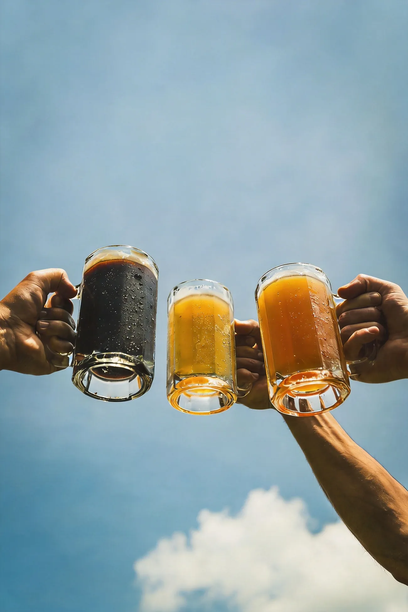 Tres jarras de cerveza Kalima, rubia, negra y roja, brindando contra el cielo